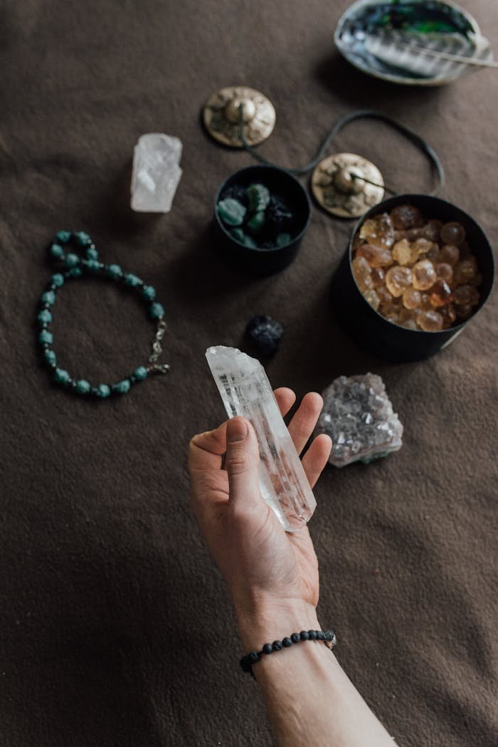 our-story-02 A hand holding a crystal with various stones and jewelry on a textured surface.
