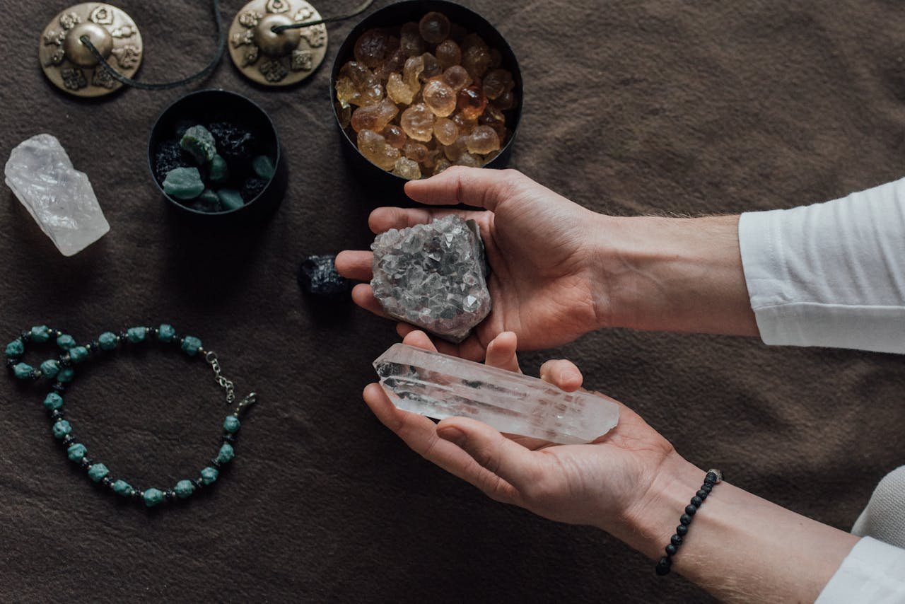 Close-up of hands holding healing crystals, surrounded by natural gemstones and a beaded bracelet.