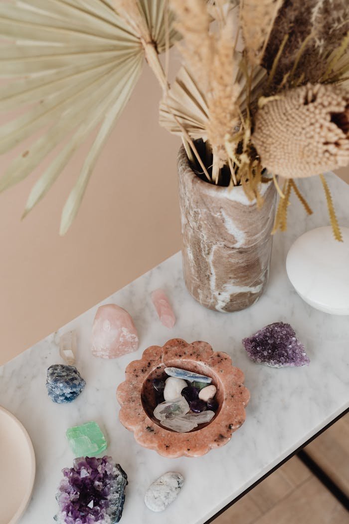 Top view of a vase with dried flowers and assorted crystals on a marble table.