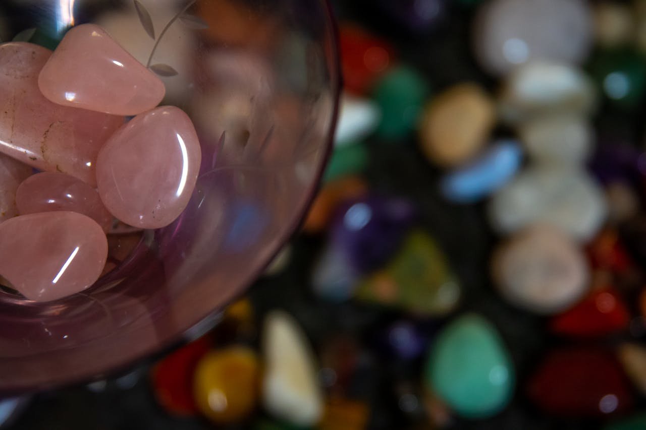 Close-up of rose quartz stones in glass with a blurred background of various colorful pebbles.